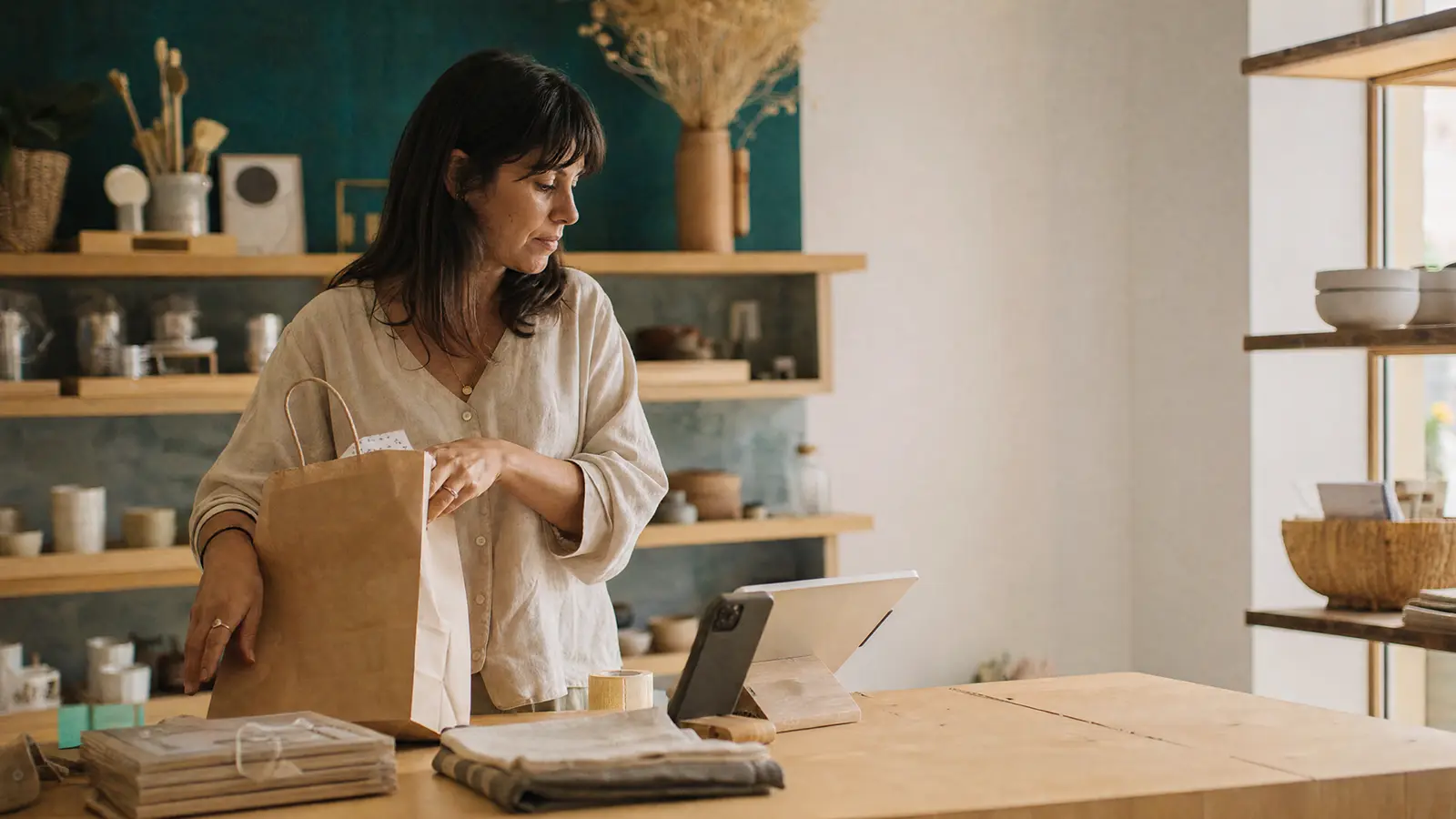 A shop owner packing an order at the counter, with a tablet running nearby.